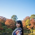 紅葉する日本庭園の池に映る紅葉を見る着物の女性 2枚目