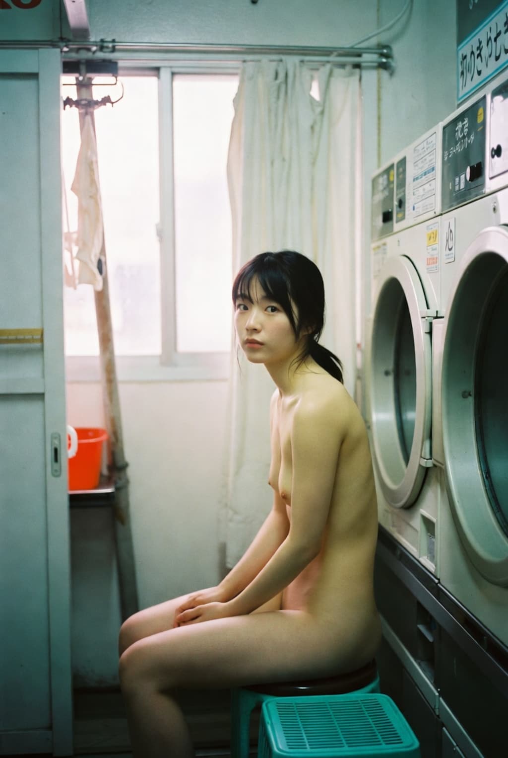 昼間のコインランドリー、自分の服が乾くまで着るものがない20歳日本女性は無着衣で洗濯機の前のイスに座って待ってる